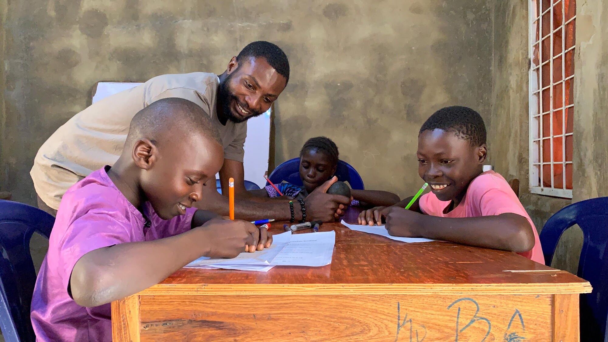 A facilitator smiling as two learners work on their writing